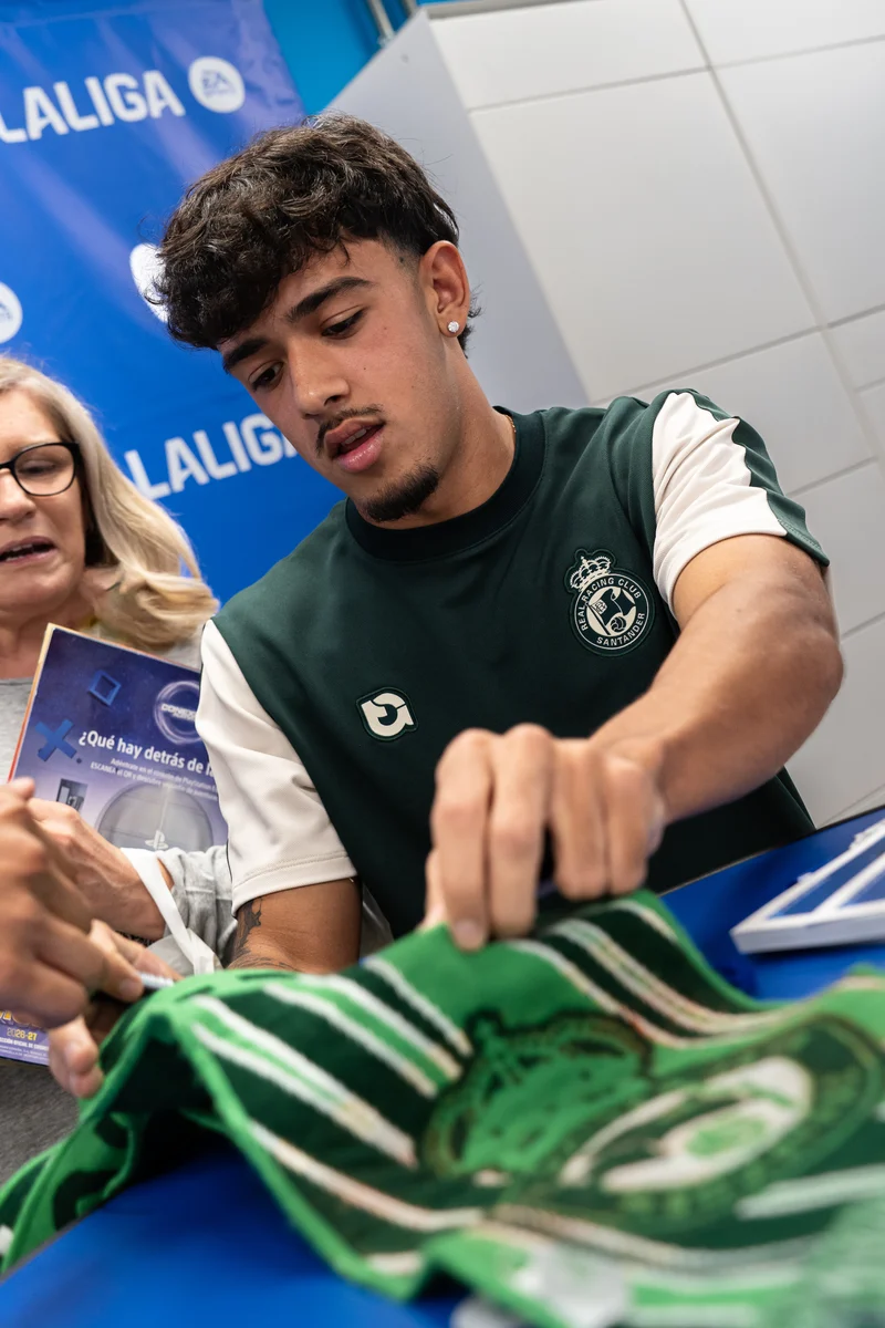 Un jugador del Racing firma una camiseta verde de un aficionado en Santander.